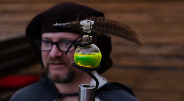 Ein Alchemist trägt einen Flakon mit giftgrünem Elixier
